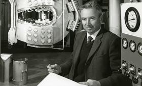 B&W photo of Richard Post sitting next to giant magnet